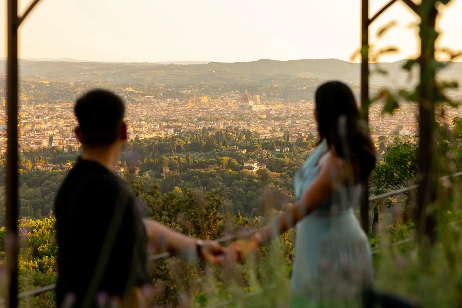 Pooja and Barun in silhouette on a terrace above Florence at dusk, the city spread out below them