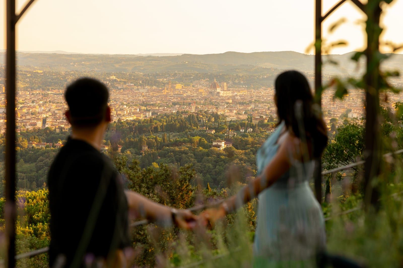 Pooja and Barun in silhouette on a terrace above Florence at dusk, the city spread out below them